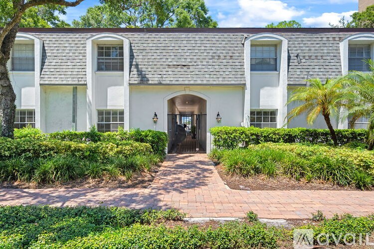 A white house with a black door and windows surrounded by greenery.