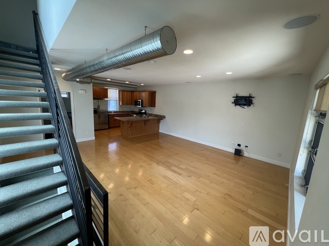 A spacious room with wooden flooring and a staircase on the left side.