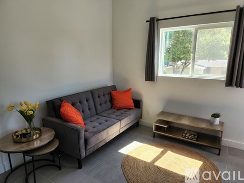 A living room with a grey sofa, a coffee table, and a window with a view of trees.