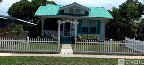 A green house with a white picket fence in front.