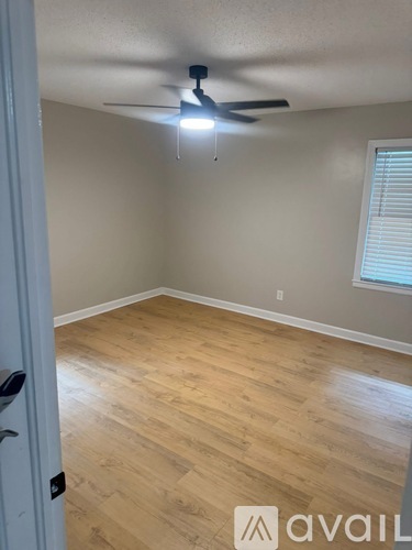 A room with a ceiling fan and light, wooden flooring, and a window with blinds.