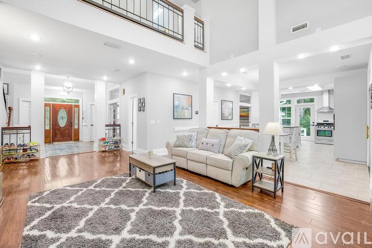 A spacious living room with a large rug in the center and a kitchen area in the background.