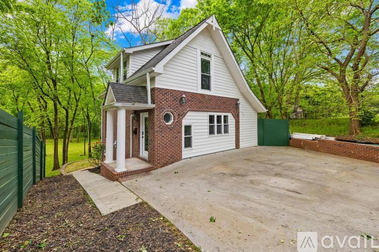 A white house with a brick chimney is surrounded by a green fence.