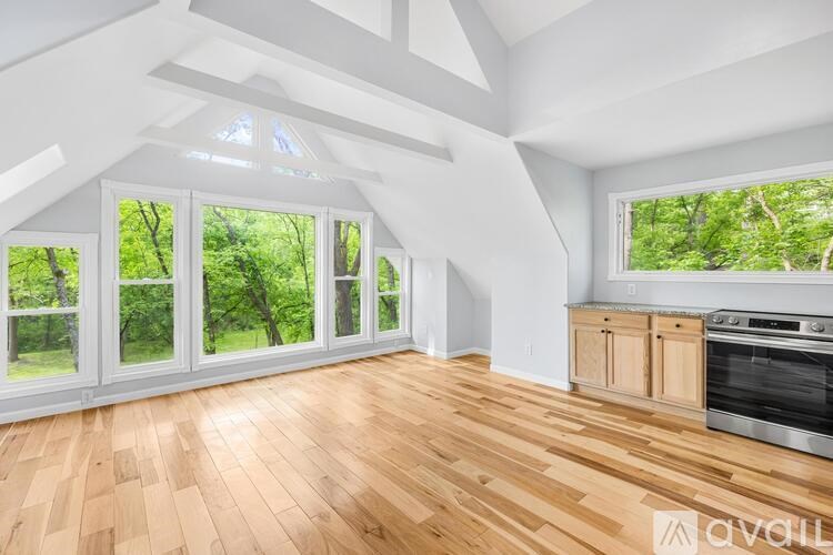 A spacious room with wooden floors and large windows overlooking a green landscape.
