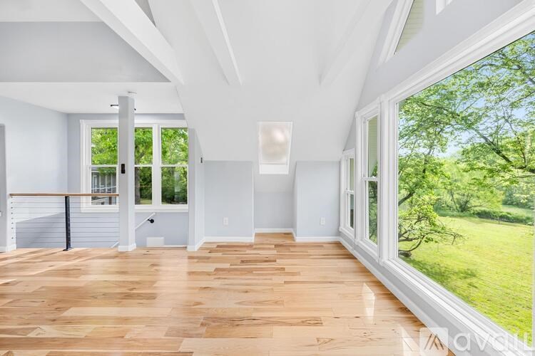 A spacious room with wooden floors and large windows overlooking a green lawn.