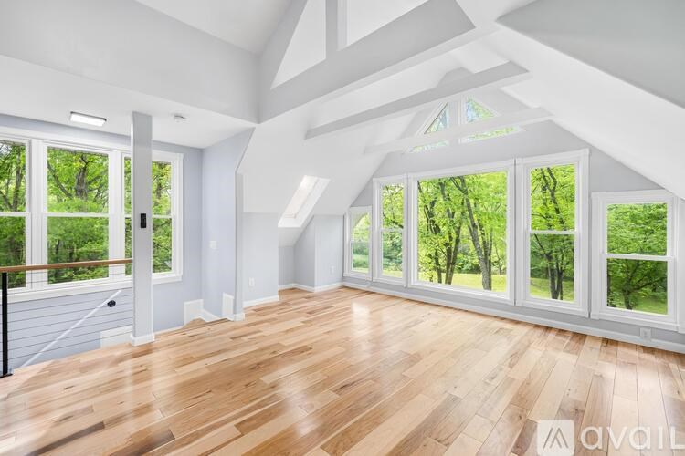 A spacious room with wooden floors and large windows overlooking a green landscape.