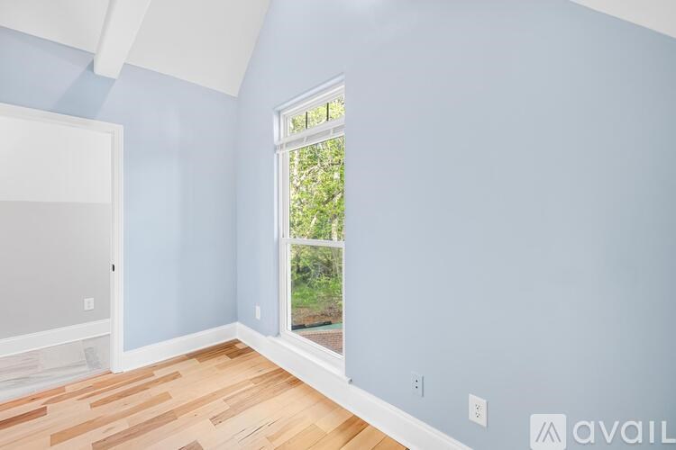 A room with light blue walls and wooden flooring with a window that shows greenery outside.