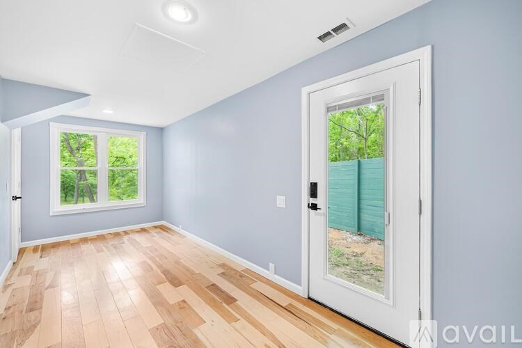 A room with light blue walls and wooden flooring, with a white door leading outside.
