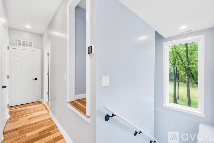 A hallway with a white door and a window with a view of trees outside.