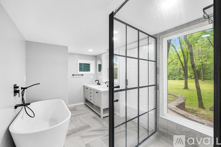 A bathroom with a tub, sink, and window overlooking a garden.