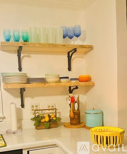 A kitchen with a white counter top and wooden shelves with various items on them.