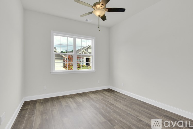 A room with a ceiling fan and a window showing a view of a house.