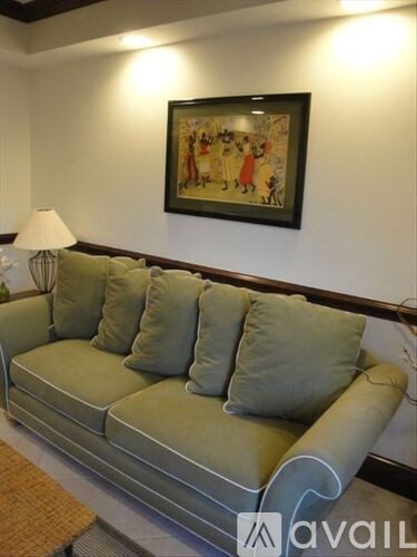 A living room with a green couch and a painting on the wall.