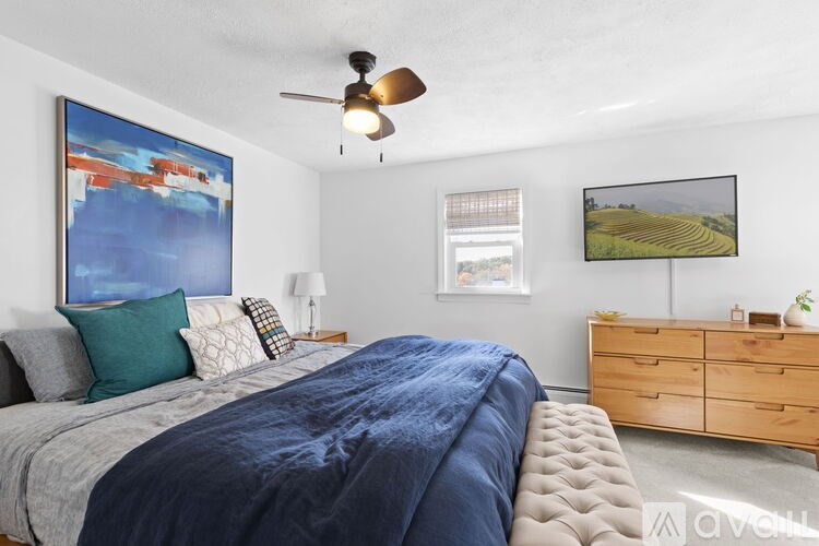 A bedroom with a bed, a ceiling fan, and a painting on the wall.
