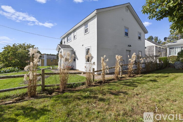 A house with a white siding and a grey roof is surrounded by a grassy area and a wooden fence.