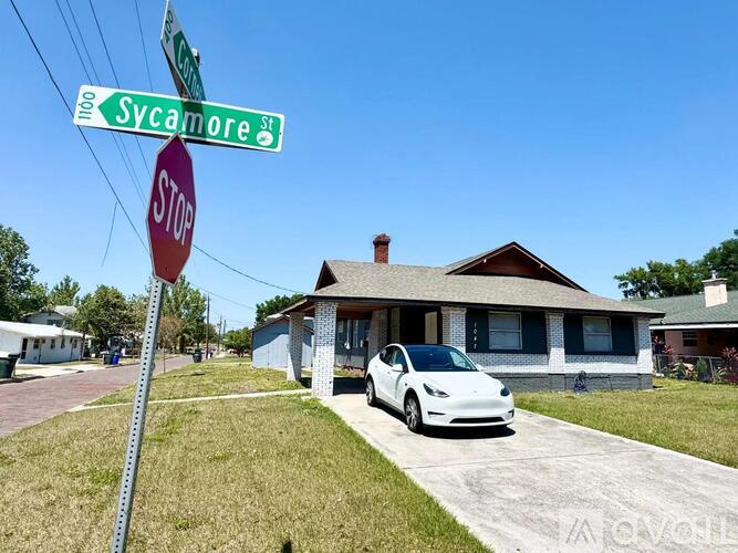 A white Tesla car is parked in front of a house on Sycamore Street.