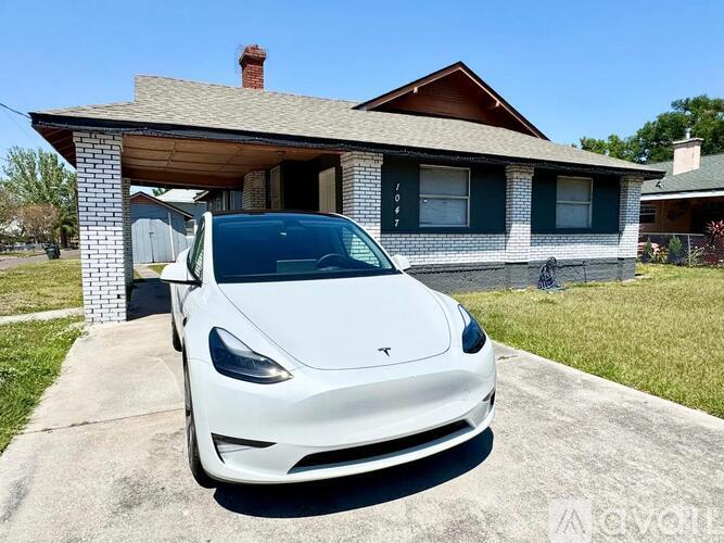 A white Tesla car is parked in front of a house.