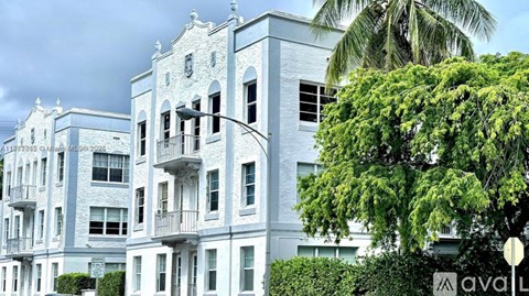 A white building with balconies and a tree in front.