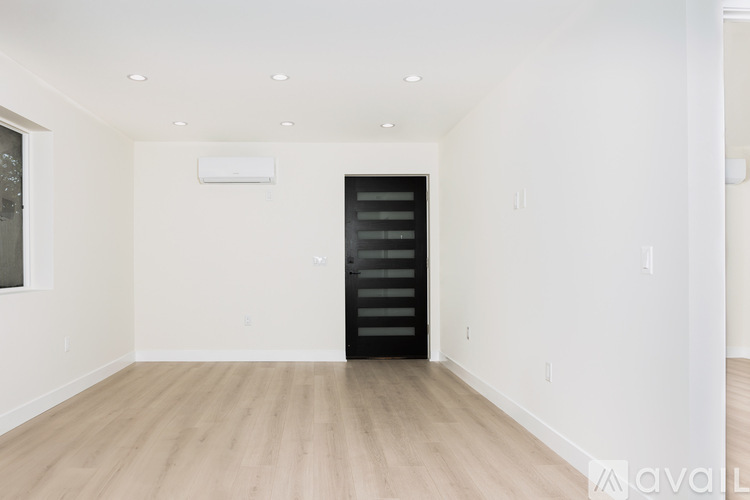 A spacious room with wooden flooring and a black door.