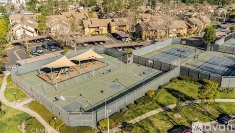 An aerial view of a tennis court surrounded by a fence and a parking lot.