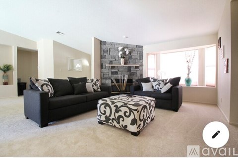 A living room with a black couch and a patterned ottoman.