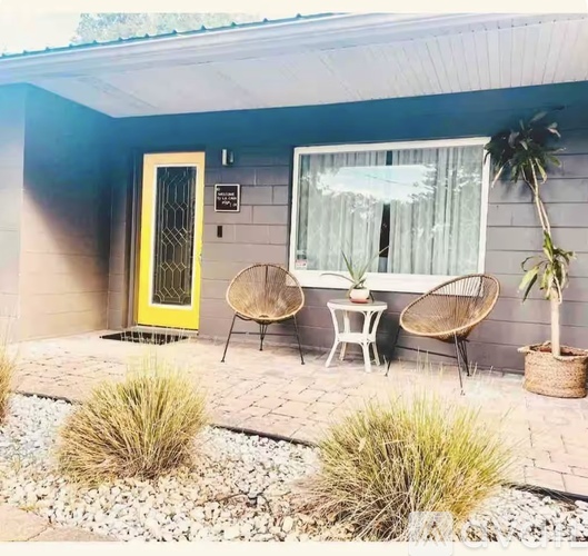 A yellow door is on the left of a grey wall with a window and two chairs.