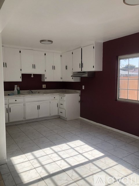 A kitchen with white cabinets and a red wall.