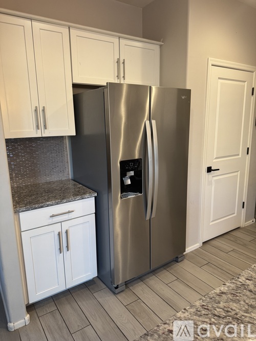 A stainless steel refrigerator with a digital display on the door stands in a kitchen with white cabinets.