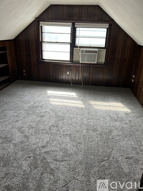 A room with a carpeted floor and a window with a fan.