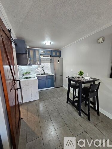 A kitchen with a refrigerator, sink, and a dining table with chairs.