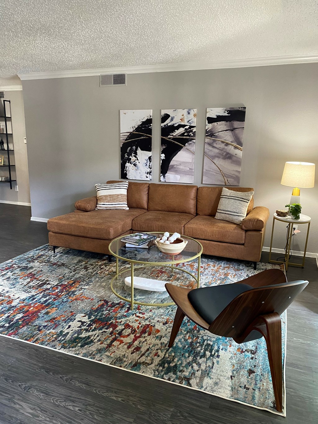 A living room with a brown couch, a glass coffee table, and a colorful rug.