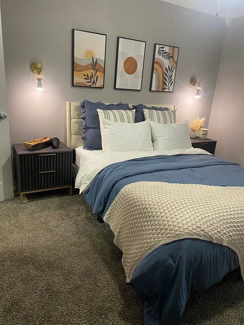 A bedroom with a bed, nightstand, and wall art.