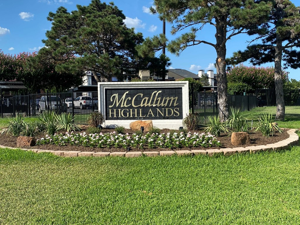 A sign that says "McCallum Highlands" is surrounded by a flower bed and trees.