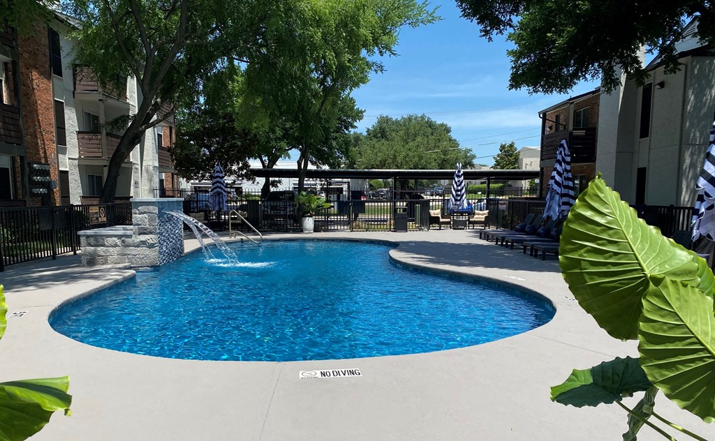 A blue swimming pool surrounded by trees and buildings.