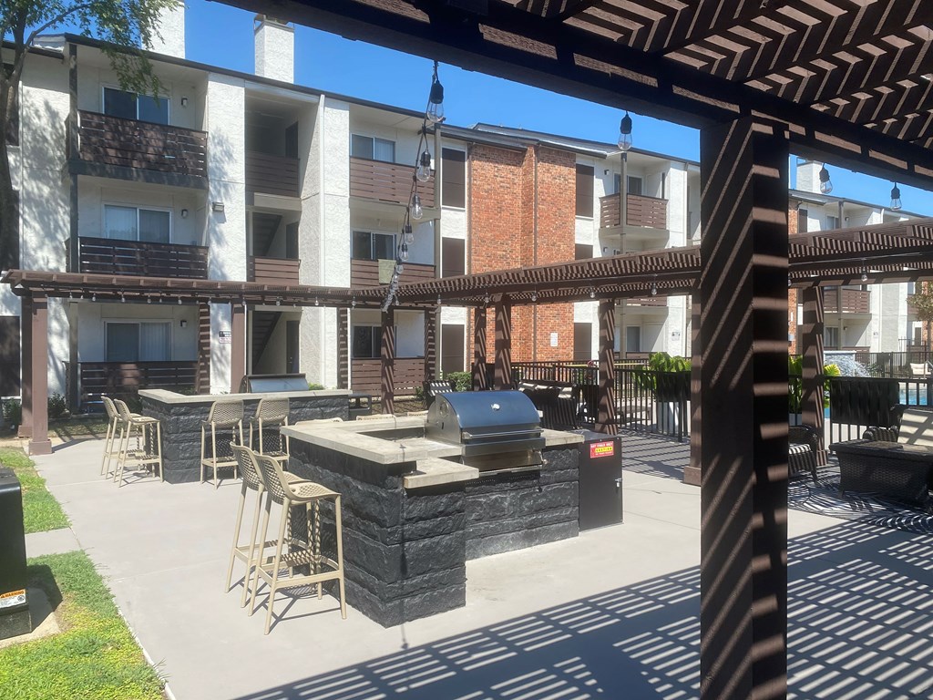A patio with a barbecue grill and chairs is surrounded by apartment buildings.