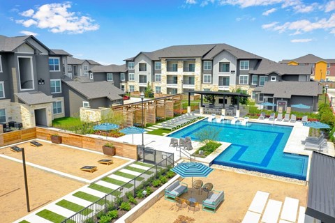 A large swimming pool surrounded by a fence and a patio area with chairs and a table.