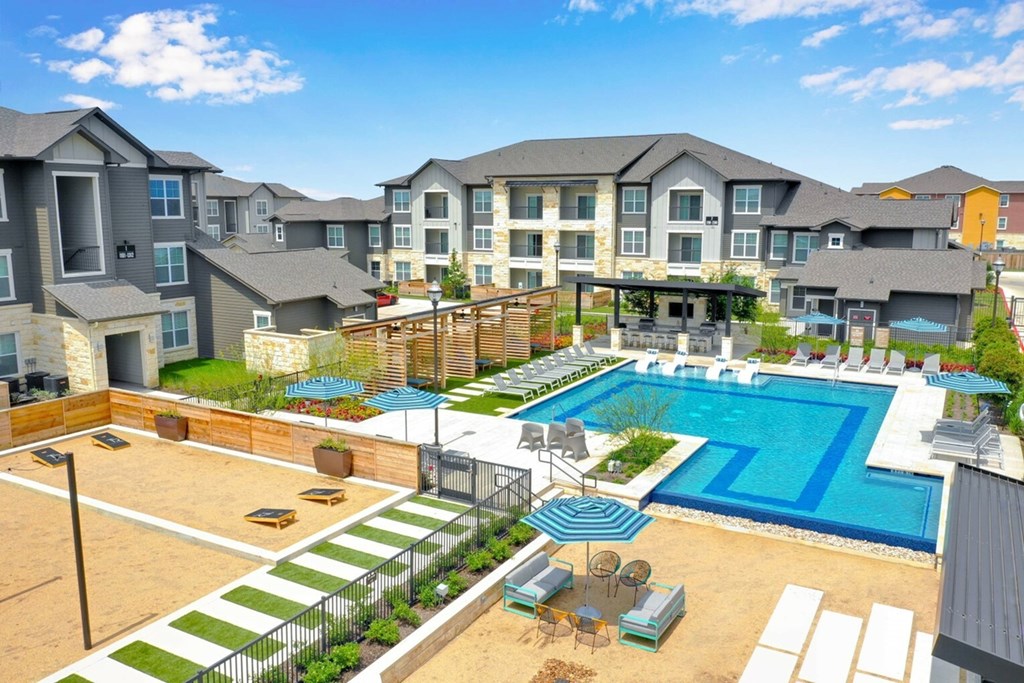A large swimming pool surrounded by a fence and a patio area with chairs and a table.