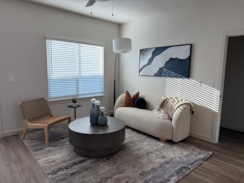 A living room with a white couch, a wooden chair, a round table with a vase and a plant on it, and a painting on the wall.