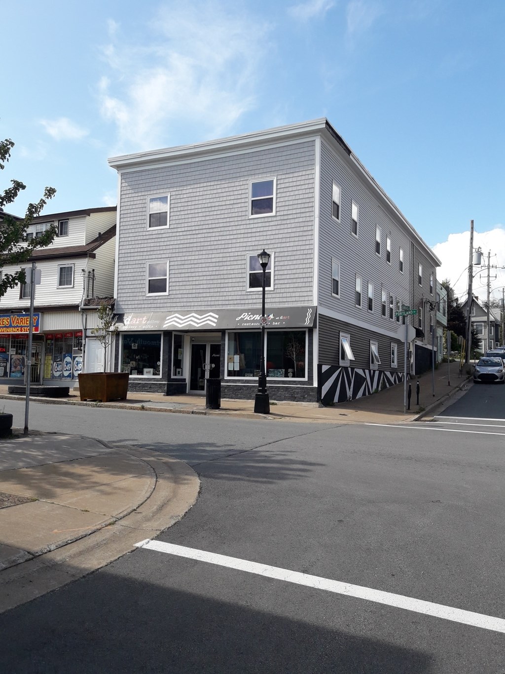 A grey building with a black and white striped awning sits on a street corner.