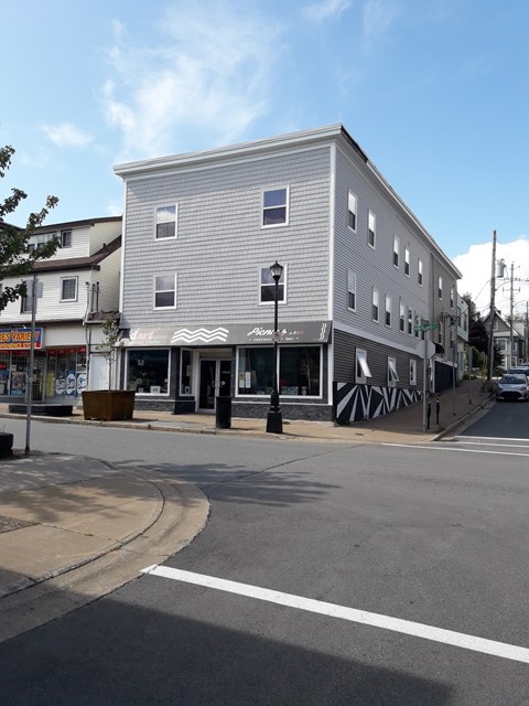 A grey building with a black and white striped awning sits on a street corner.