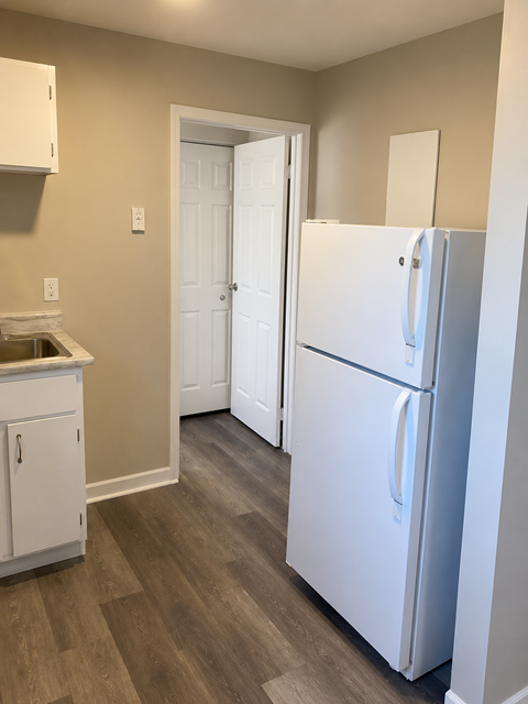 A white refrigerator stands in a kitchen with a white cabinet and a white door.