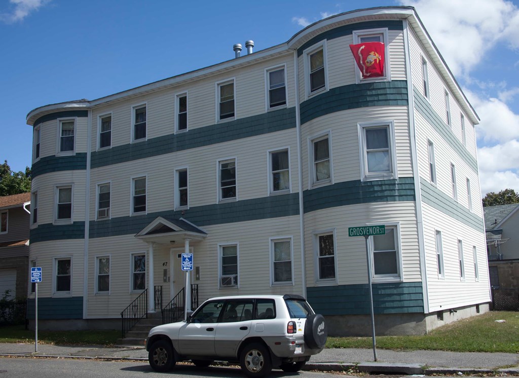 A white car is parked in front of a blue and white building.