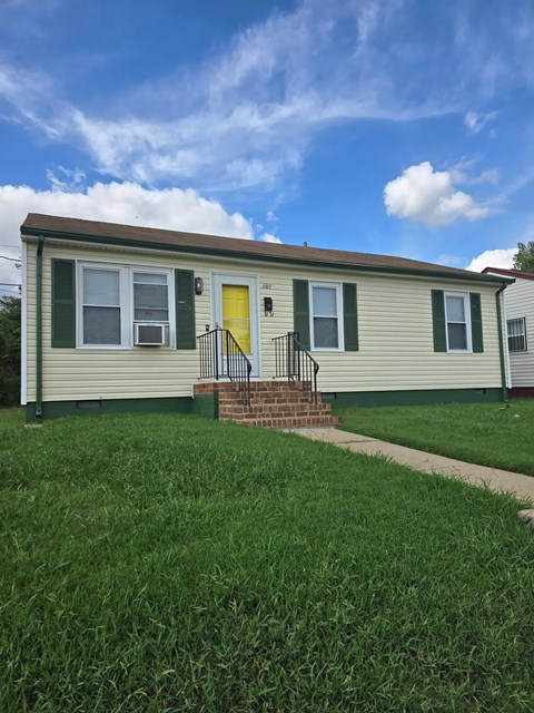 A small house with a yellow door and green shutters.