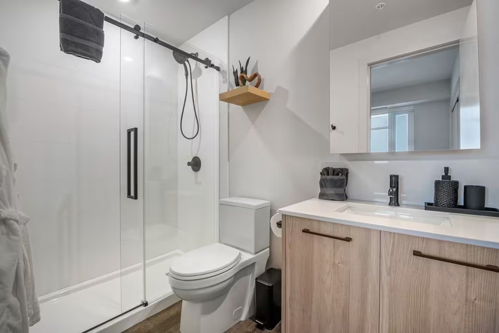 A white toilet sits in a small bathroom with a walk-in shower.