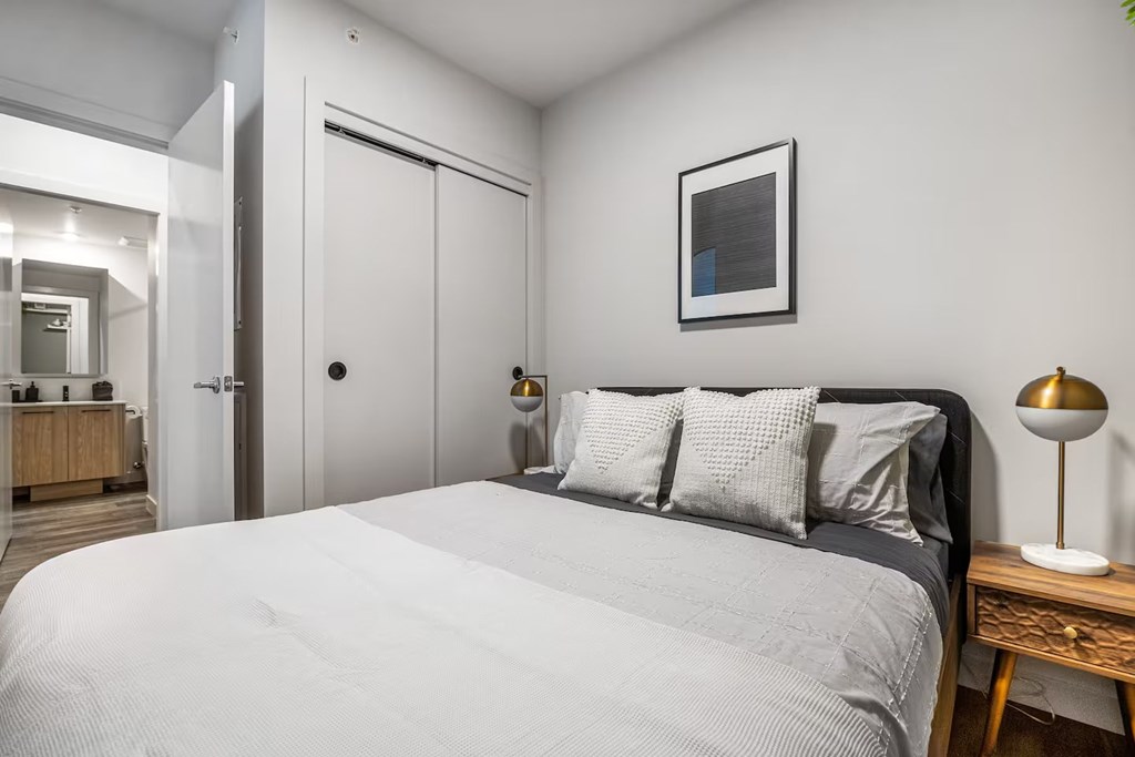 A bedroom with a large bed and a lamp on a side table.