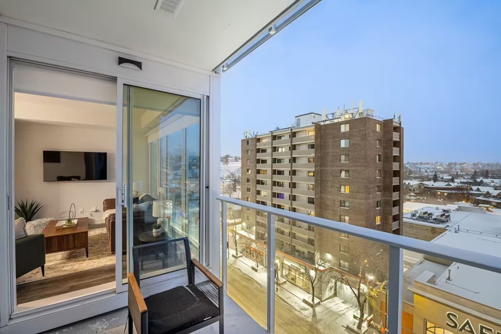 A balcony with a chair and a view of a snowy landscape and apartment buildings.