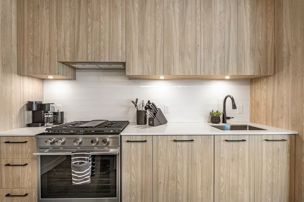 A modern kitchen with a stove top oven and wooden cabinets.