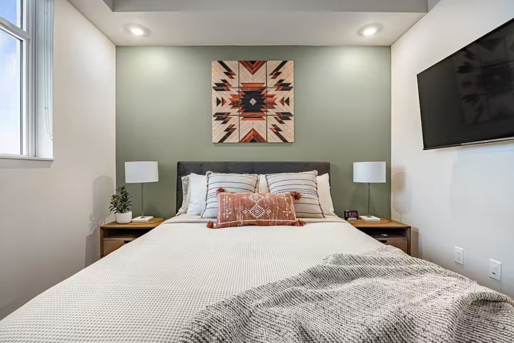 A bedroom with a large bed and a colorful tapestry on the wall.