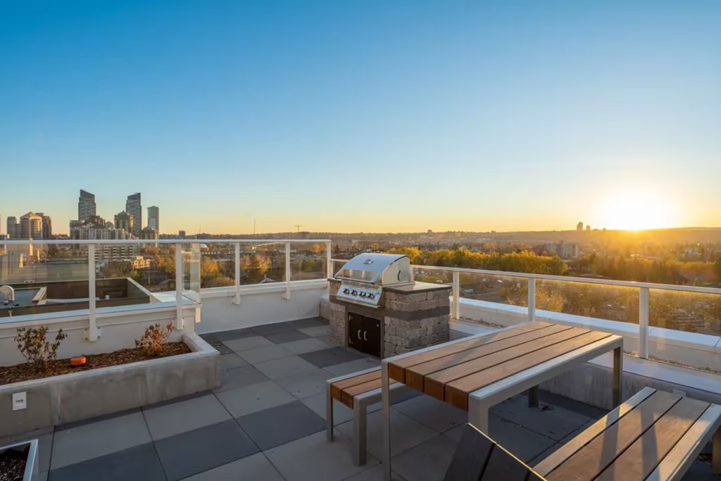 A rooftop patio with a table and chairs overlooking a city skyline at sunset.