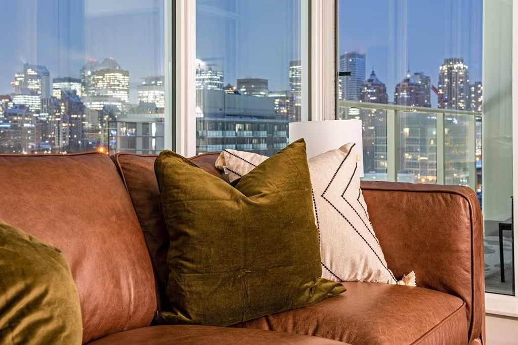 A brown couch with two pillows in front of a window with a city view.